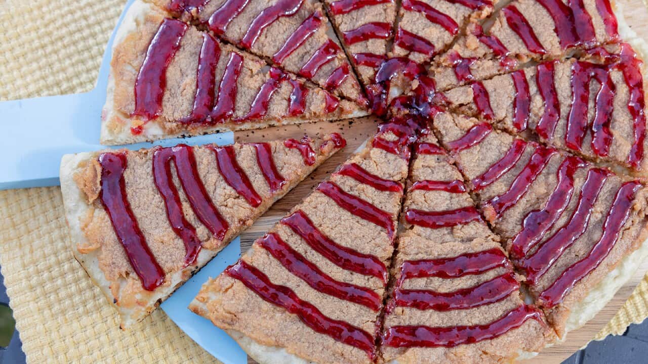 A pizza cut into 10 wedges is seen from overhead. It has a creamy-brown topping, drizzled with rings of vibrant red sauce.