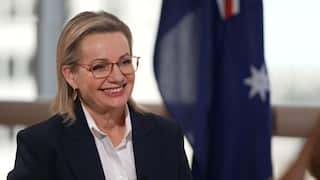 A woman wearing glasses smiles with an Australian flag in the background.