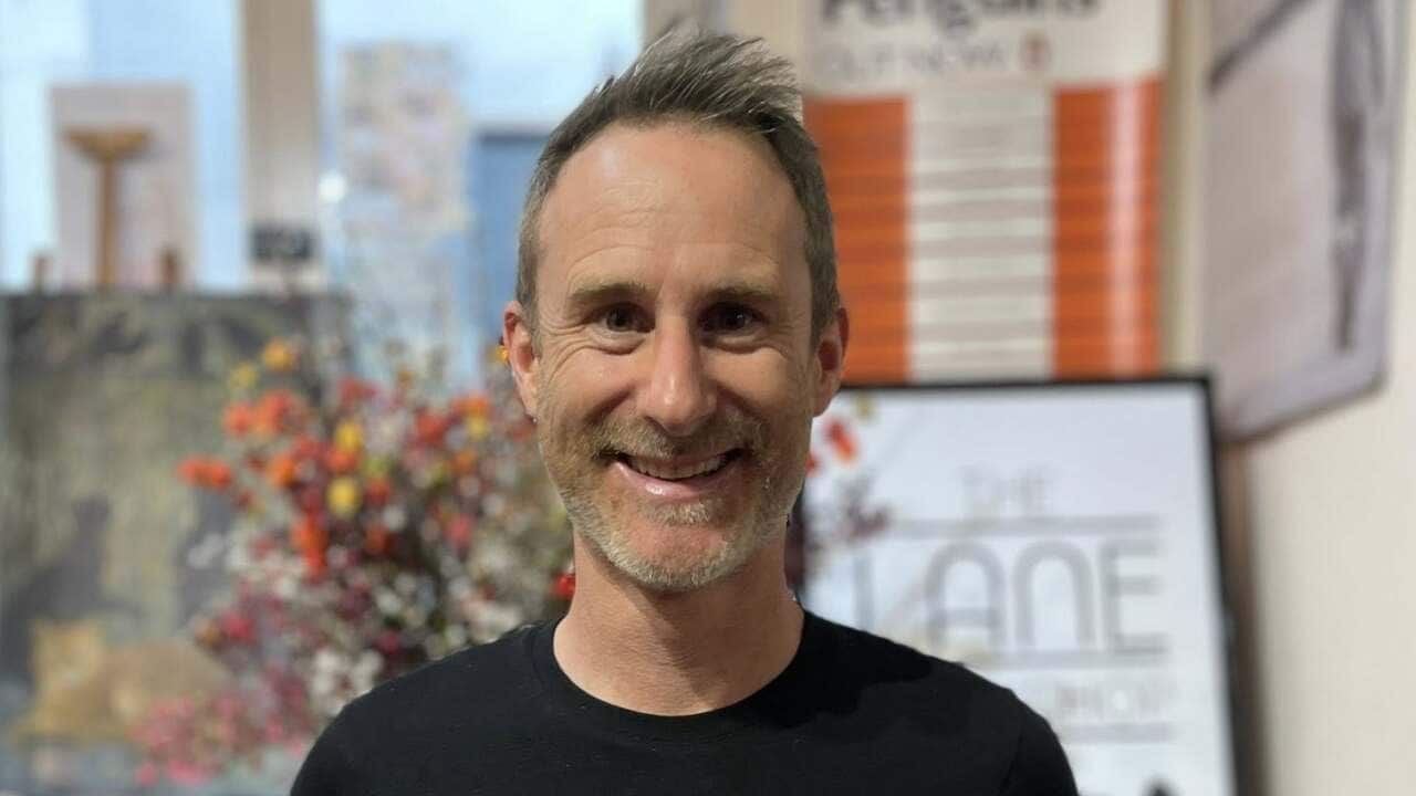 Author Craig Silvey stands in a bookstore smiling while holding two of his books, Runt and Runt and the Diabolical Dognapping.