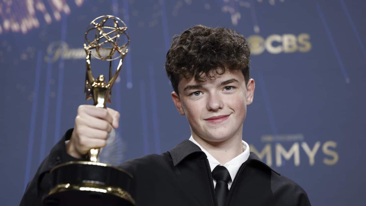A teenage boy with curly hair smiling as he holds up a trophy.