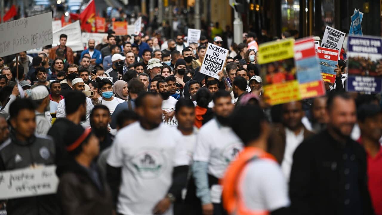A large crowd of demonstrators marching along a street. Some are holding signs