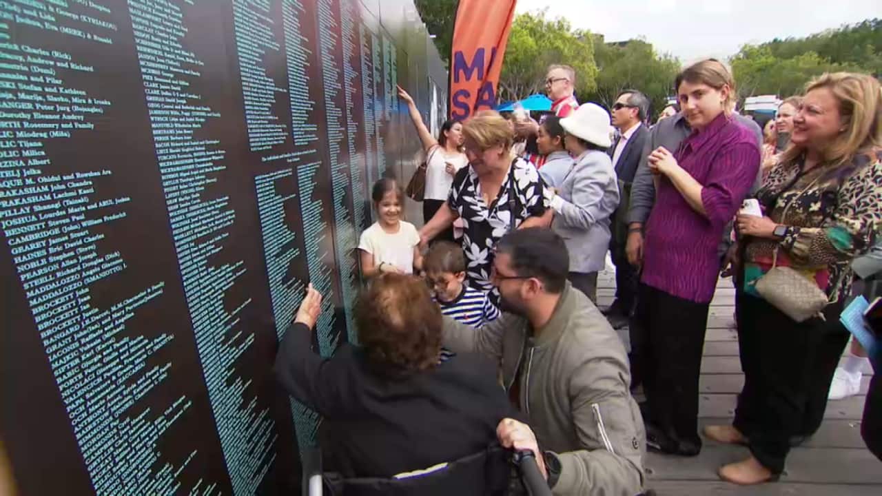 Families pointing to their names at the National Museum's Welcome Wall (SBS).png