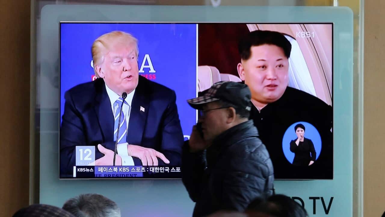 A man passes by a TV screen showing file footage of U.S. President Donald Trump, left, and North Korean leader Kim Jong-un