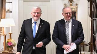 Australian Prime Minister Anthony Albanese (right) walks alongside Kevin Rudd (left) through an elegantly furnished indoor hallway. Both men are wearing dark suits and ties.