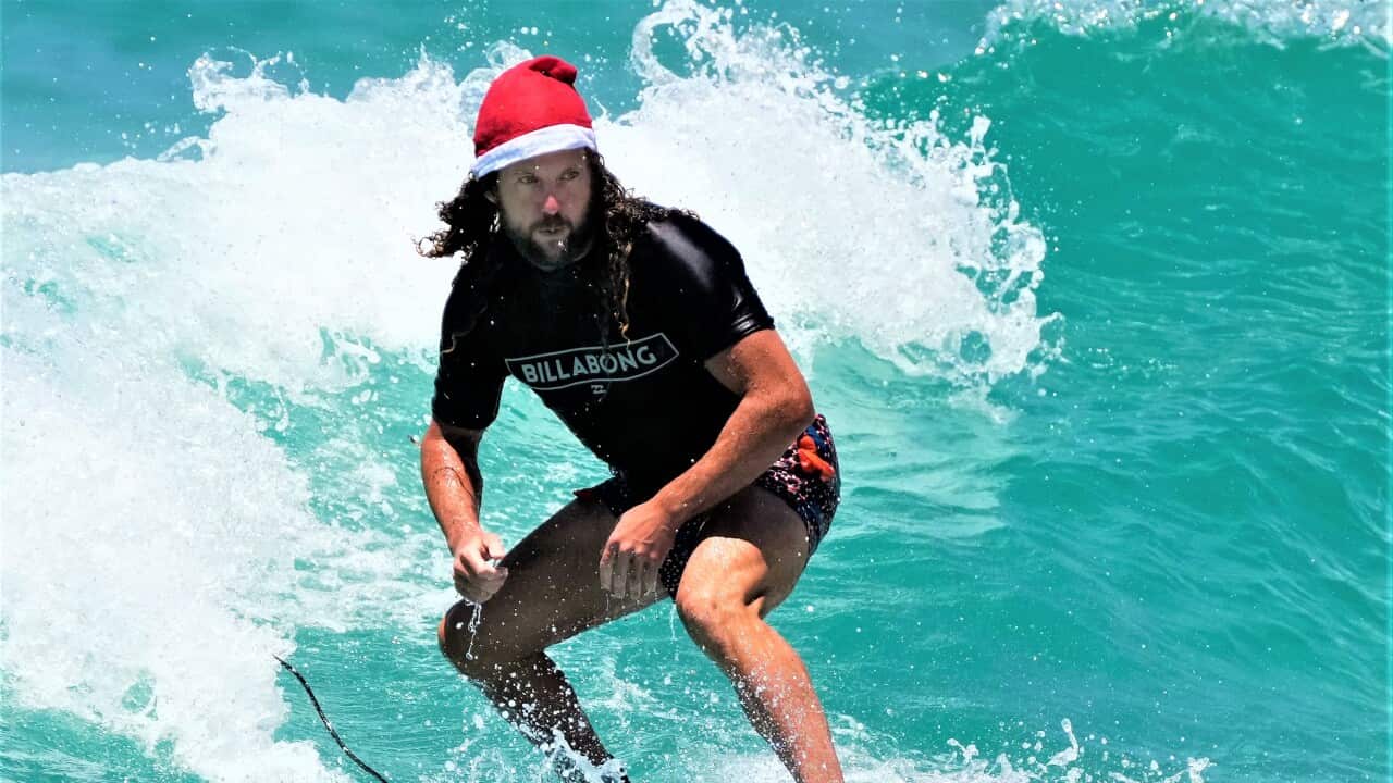 Tony O'Connor, originally from England, rides a surfboard while wearing a Santa hat as he celebrates Christmas at Bondi Beach in Sydney, Dec. 25, 2021.