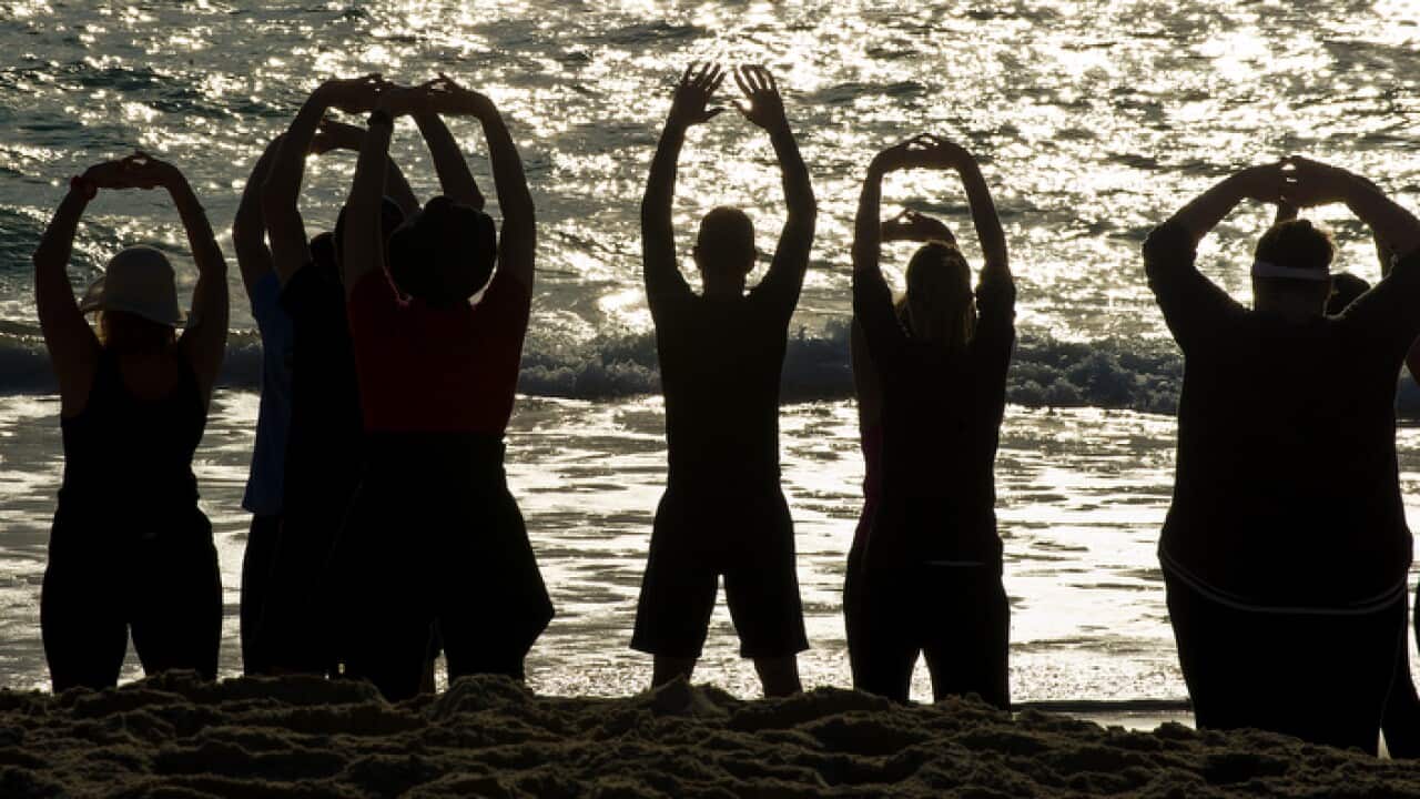 People face the ocean as they stretch during a Tai Chi exercise session