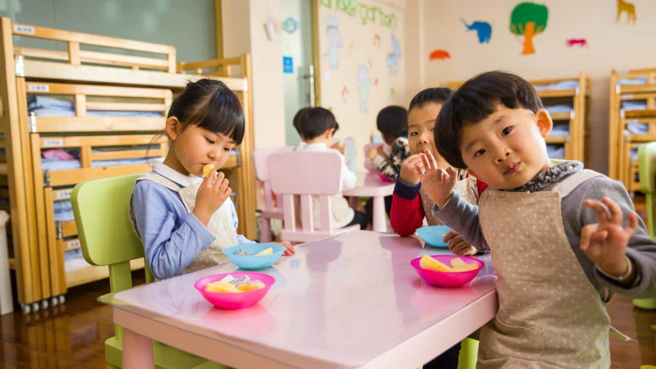 Three toddlers eating on white table.