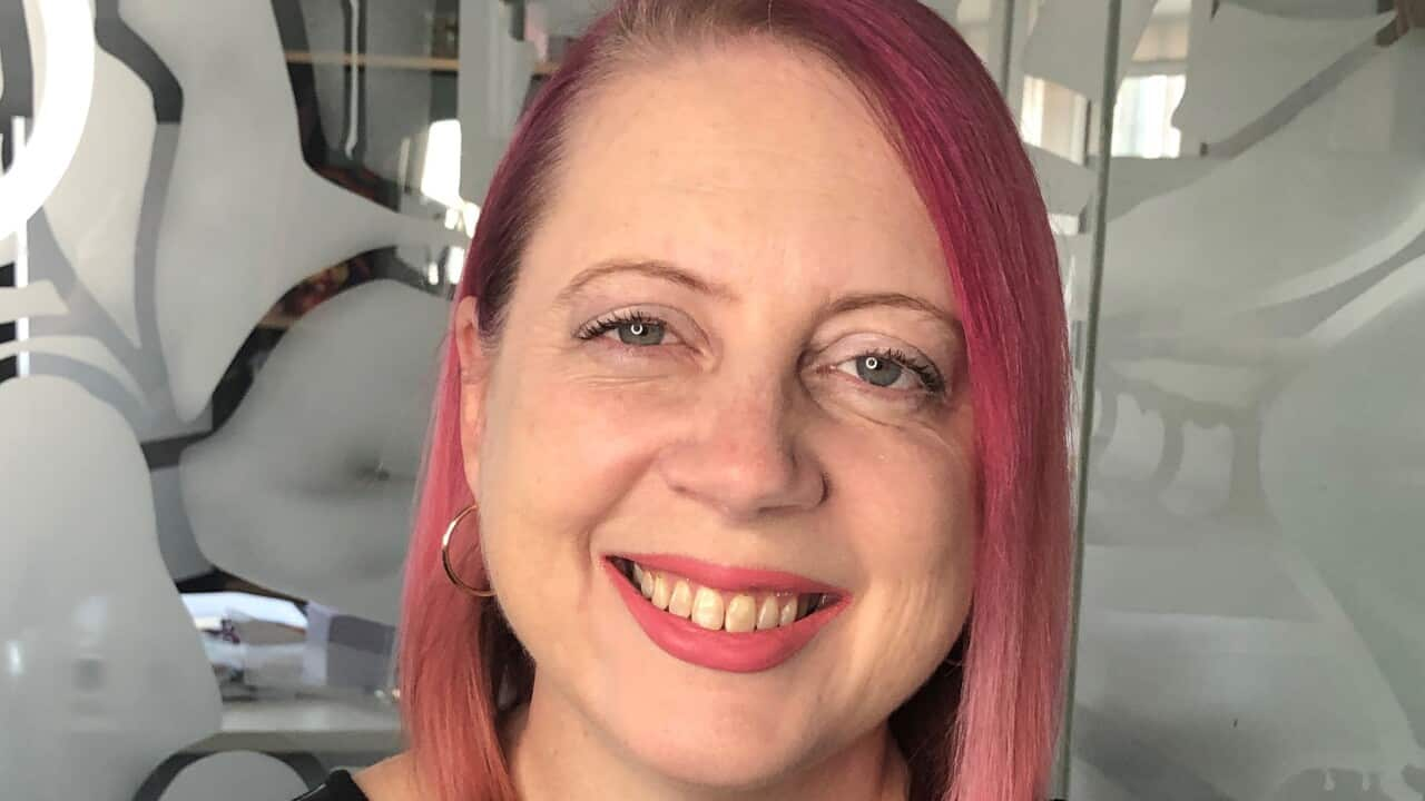 A woman with shoulder-length pink hair, smiling at the camera