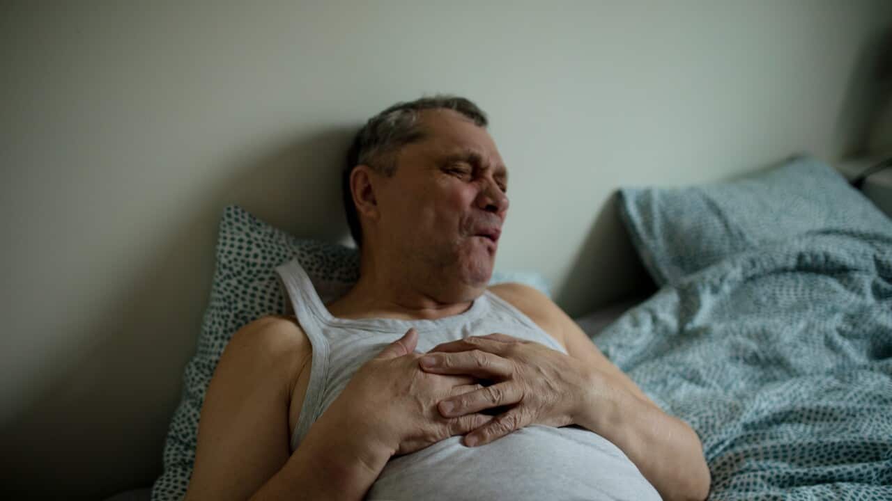 Senior man in white sleeveless t-shirt lying in bed suffering pain in chest.