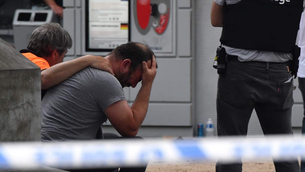 A police man stands next to a man who holds his head in his hands at the scene of a shooting in Liege, Belgium, Tuesday, May 29, 2018.