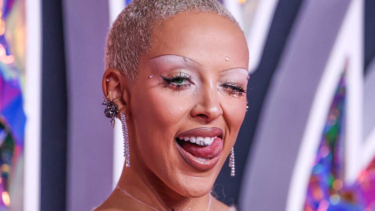 A woman with theatrical makeup and earrings winking and licking her teeth