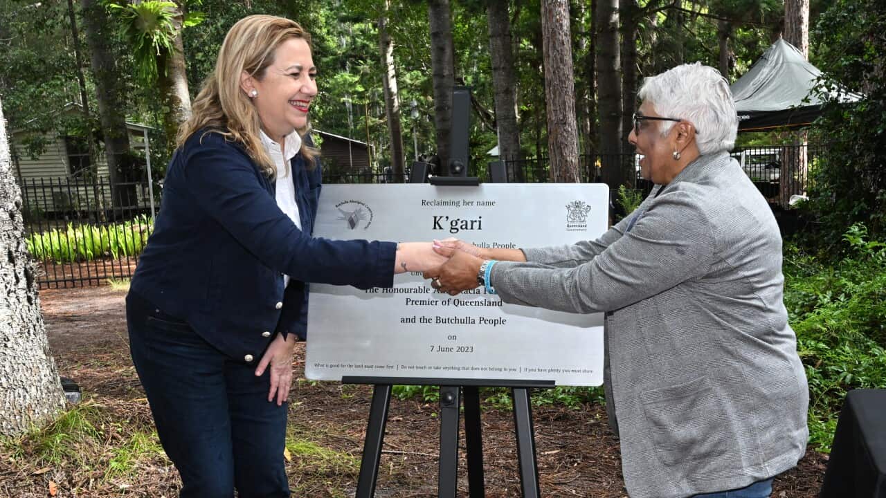Queensland Premier Annastacia Palazczuk (left), wearing a dark outfit, shakes hands with Auntie Gayle Minniecon outside. There is a large white plaque on an easel behind them.