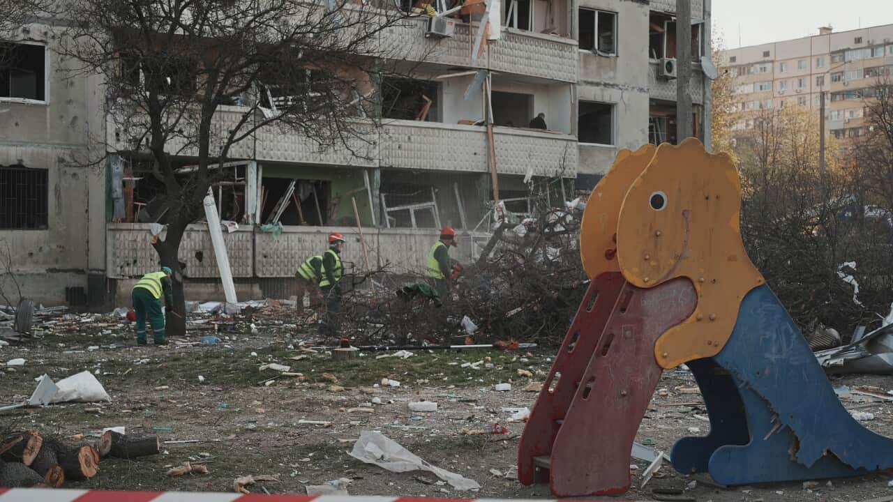 Workers clean debris near a damaged apartment block and a children's slide after an explosion or attack.