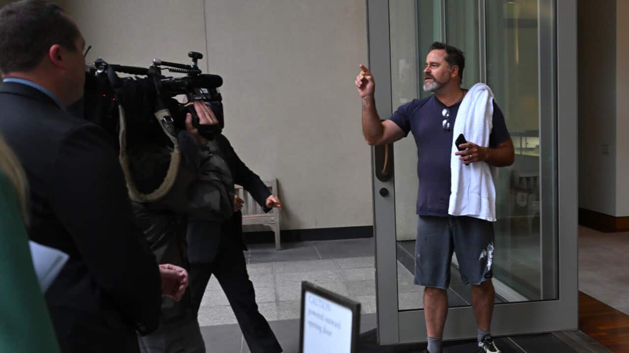 Peter Whish-Wilson, wearing grey shorts and a dark blue t-shirt and with a white towel over his shoulder, yells while standing by a glass door.