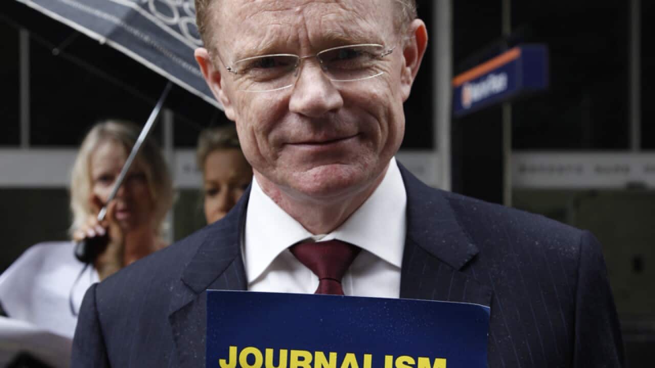 Ten News reporter Hugh Riminton holds a placard during a rally.