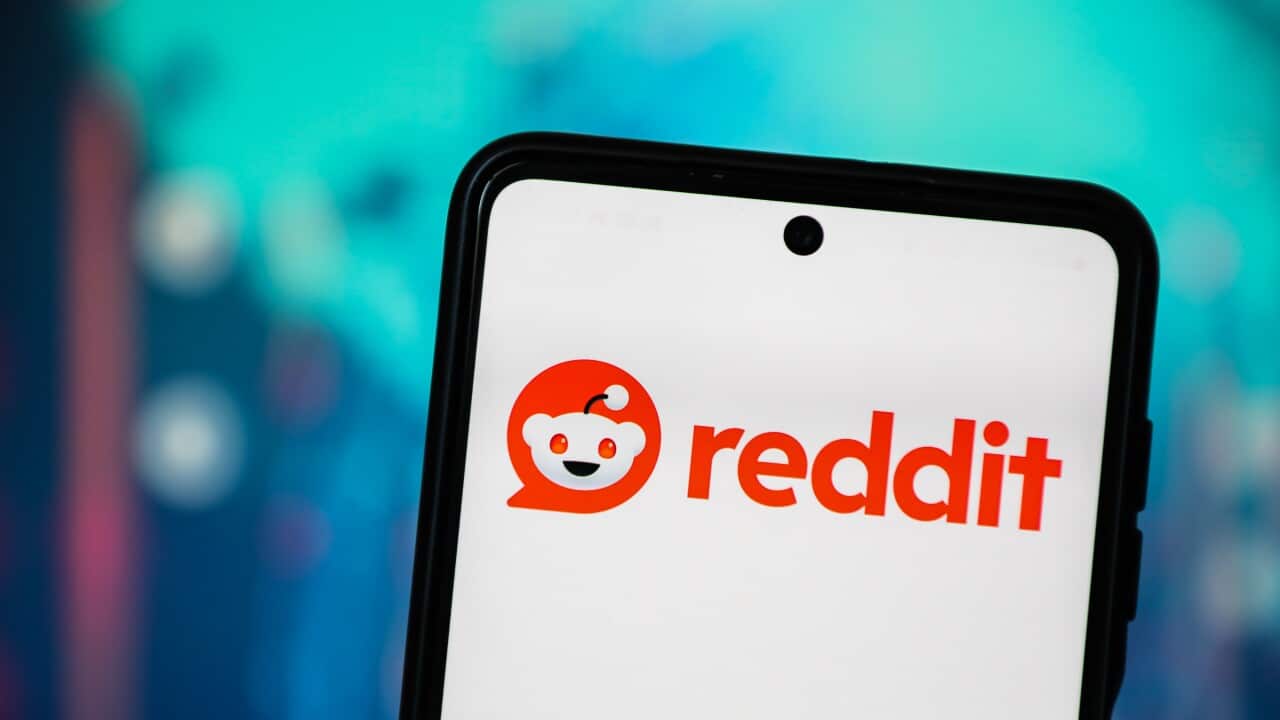 A close-up of a mobile phone showing a small alien icon and the word Reddit in red writing