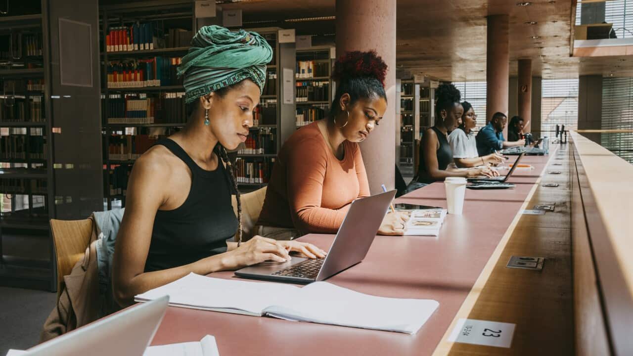 Woman wearing turban using laptop while sitting with friend in library.