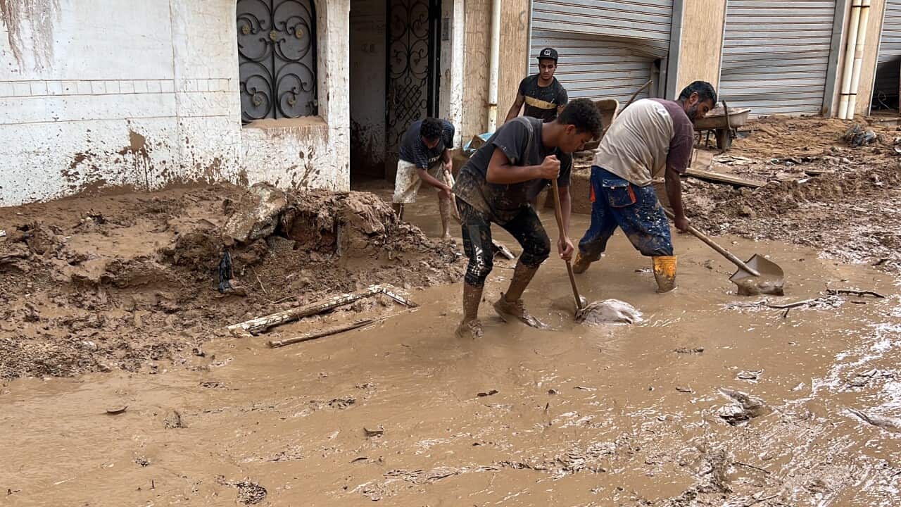 Two men with shovels try to clean a street that has been filled with mud.