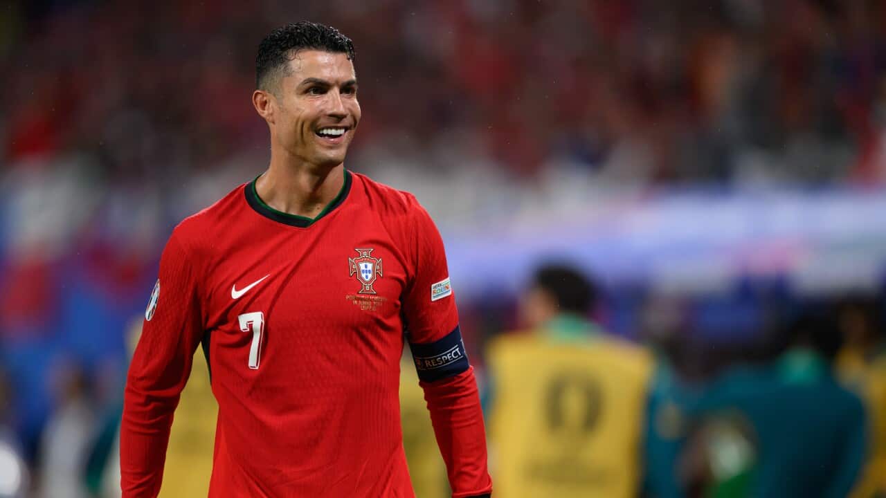 Portuguese footballer Cristiano Ronaldo smiles, wearing a red long sleeved shirt.