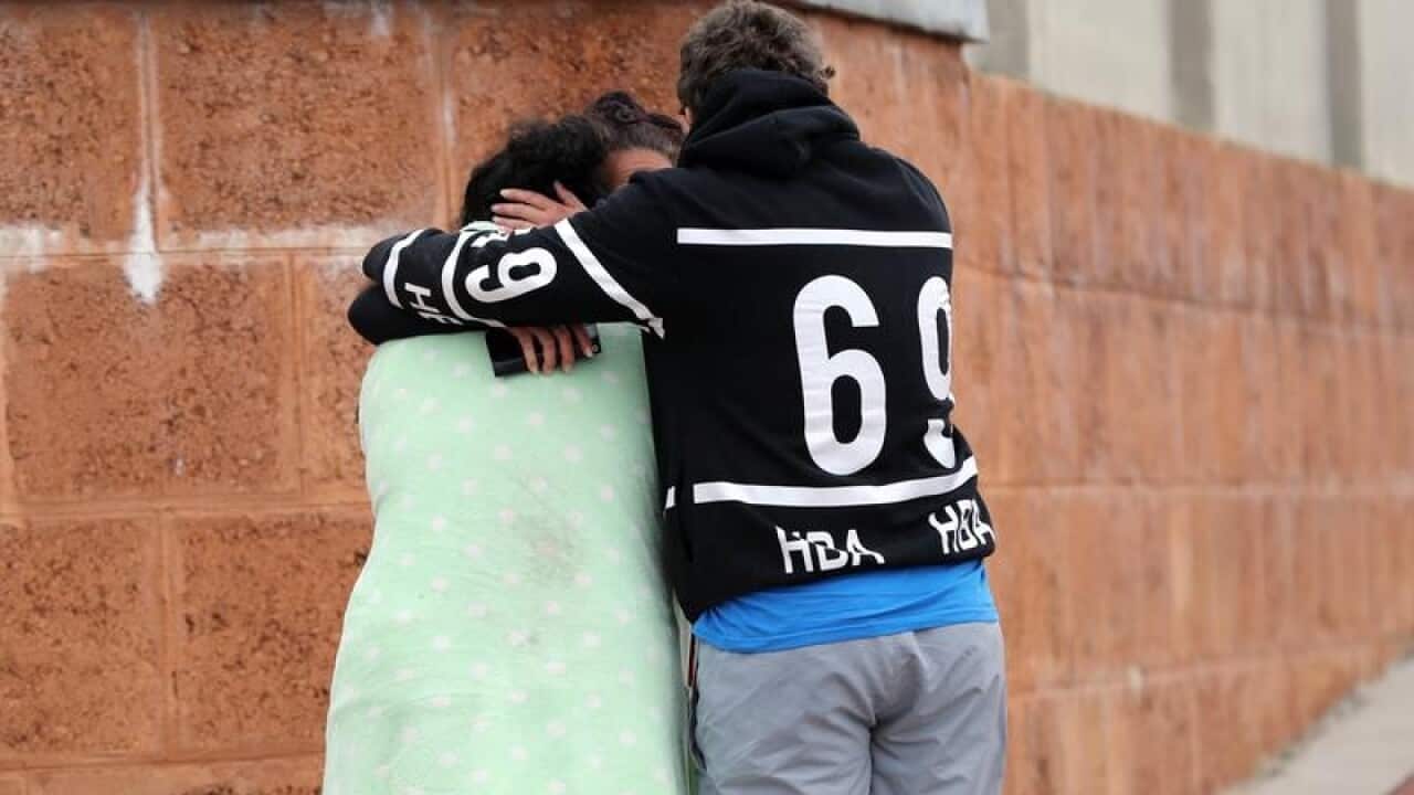 People are seen outside a house where three people died.