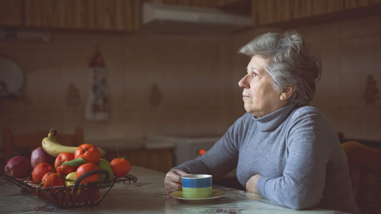 A senior woman drinking a cup of tea at her kitchen bench