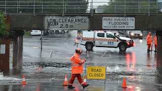 A man in a high visibility outfit on a flooded road with a "road closed" sign.