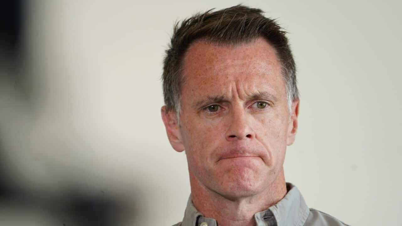 A middle-aged man with short, dark hair and a sombre expression looks slightly off-camera while wearing a grey button-down shirt.