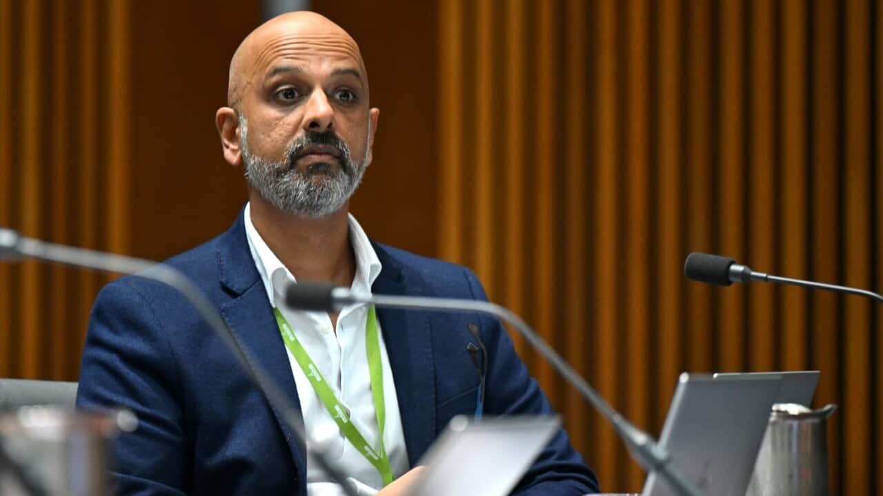 A man in a blue suit sits in front of some microphones