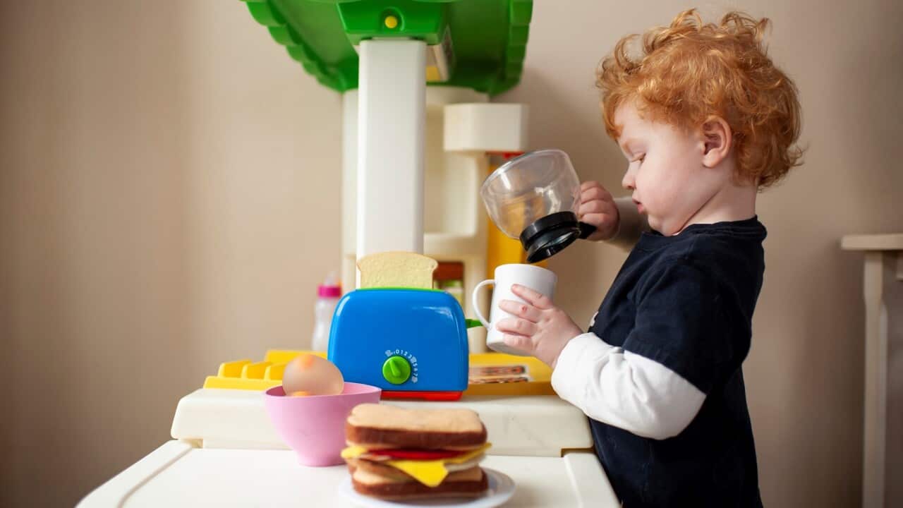 Toddler boy playing in toy kitchen pretending to pour coffee into cup
