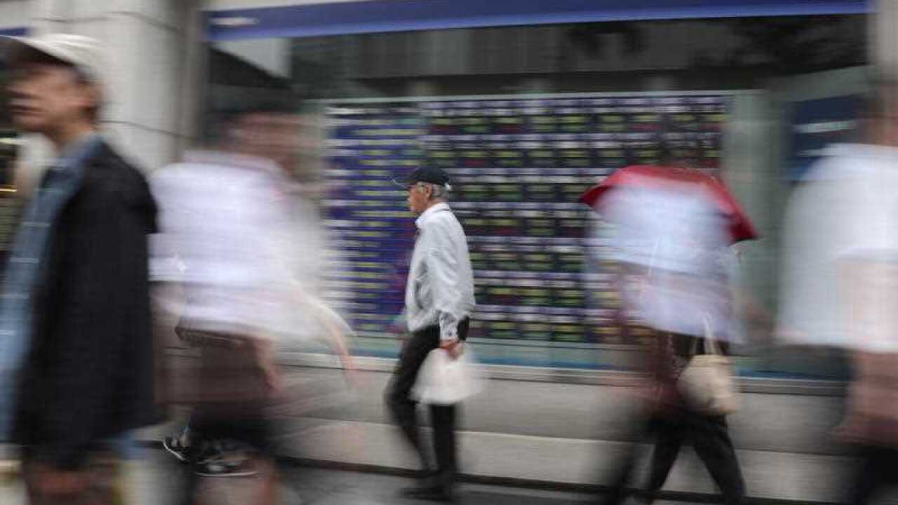 people walk past an electronic stock indicator