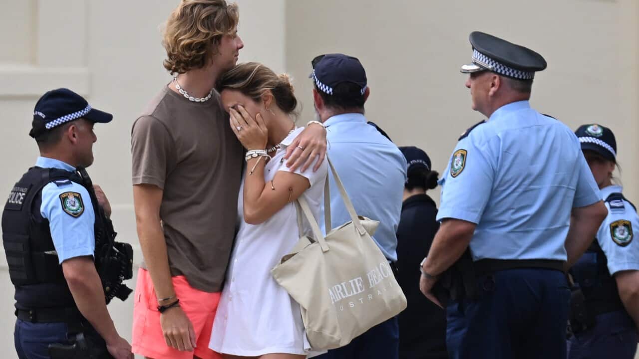 A man comforting a woman, while several police officers stand near them.