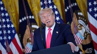 Donald Trump speaking at a podium. Behind him are flags.
