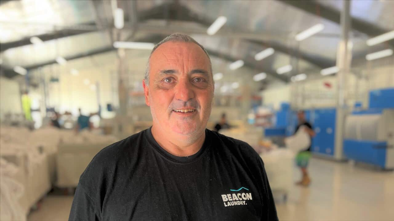 A man in a black t-shirt standing inside a laundry warehouse and smiling at camera.