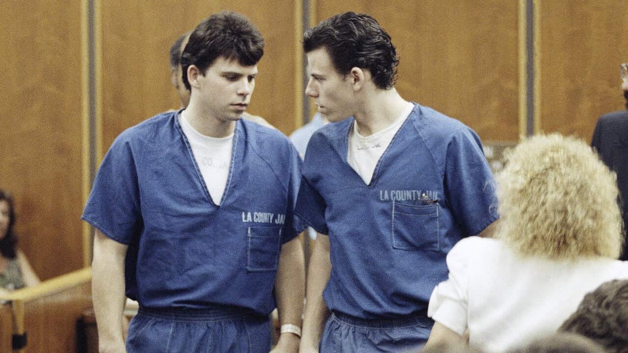 Two men dressed in prison suits are standing in a courtroom.