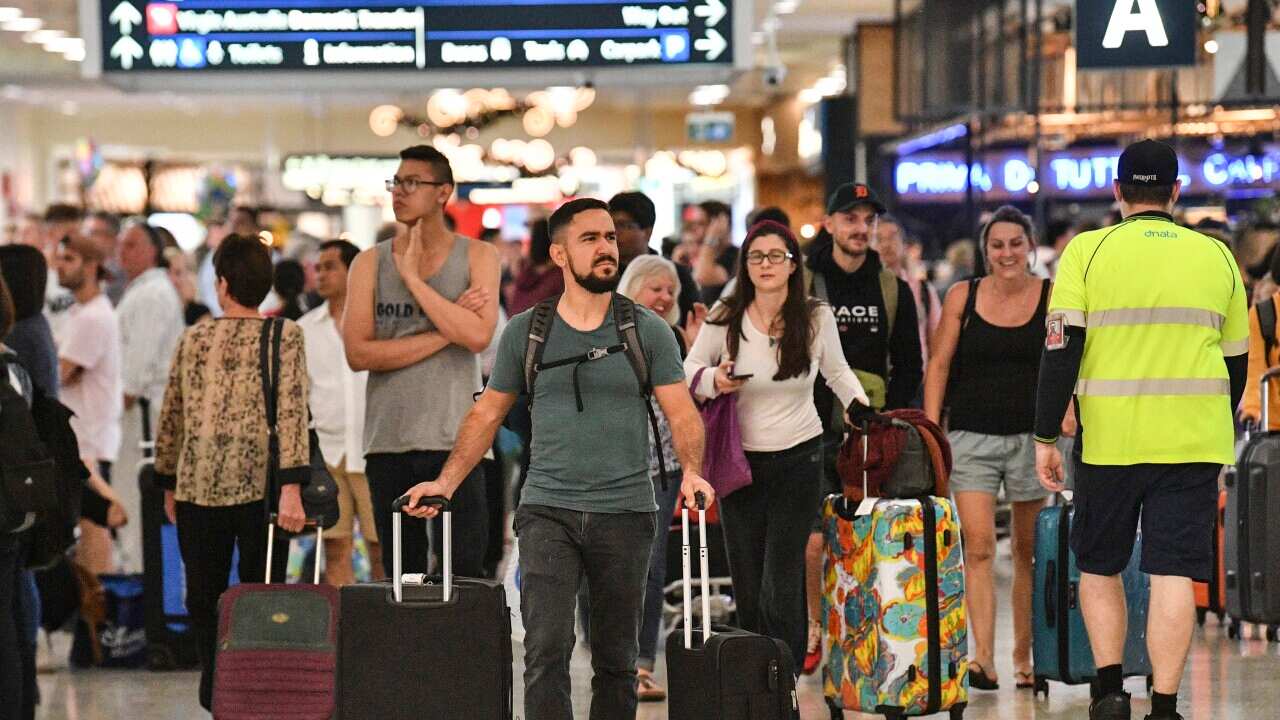 People walking through the arrivals and departures hall of an airport. Some are wheeling suitcases.