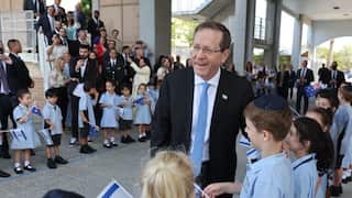 A man in a black suit with a blue tie, greeting children waving the Israeli flag.