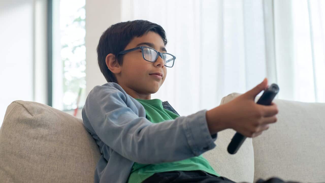 A boy sitting on a couch holding a TV remote