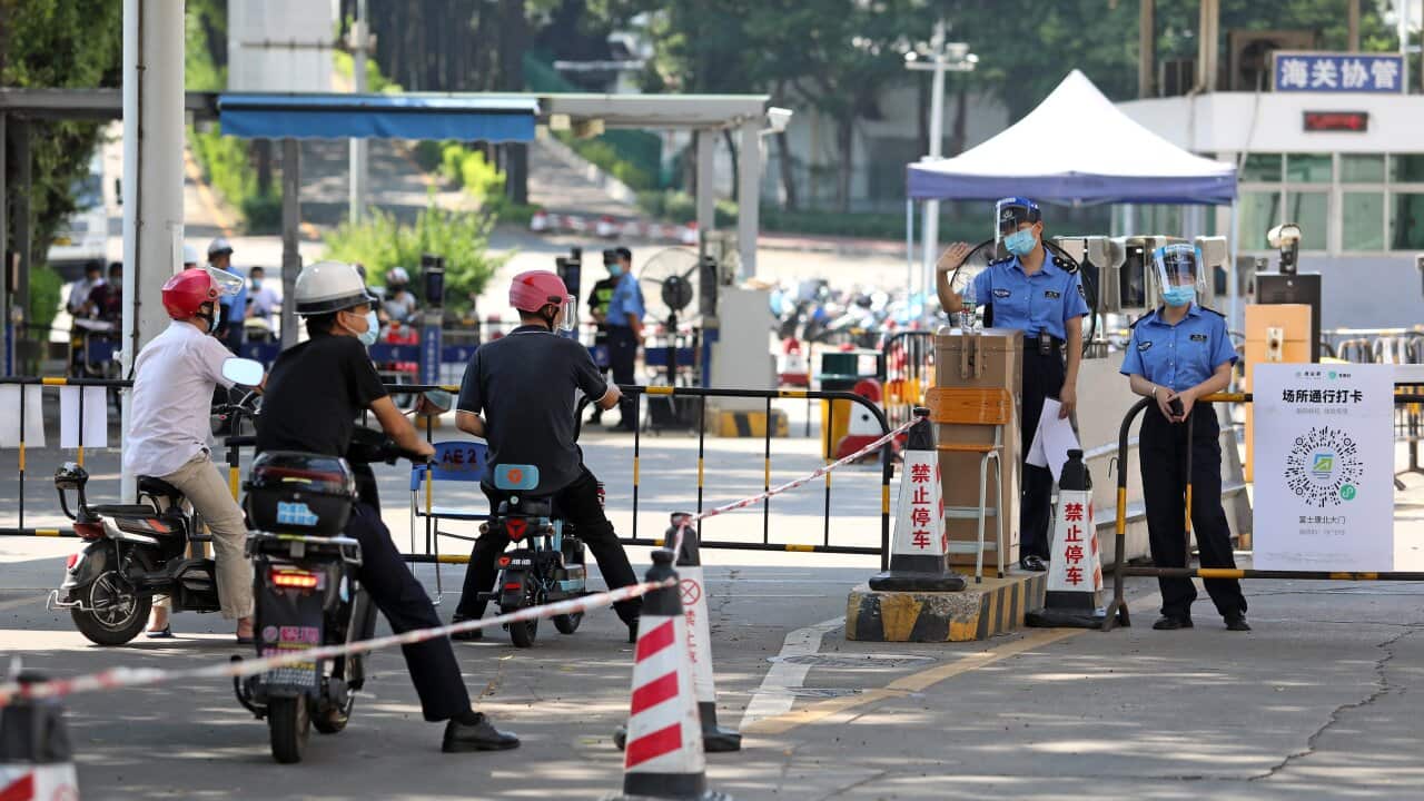 People on motorbikes at an entrance to the Foxconn plant in Shenzhen where security guards are standing.