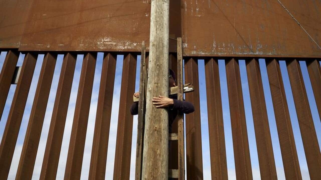 A file image of a man using a ladder to scale the existing border wall