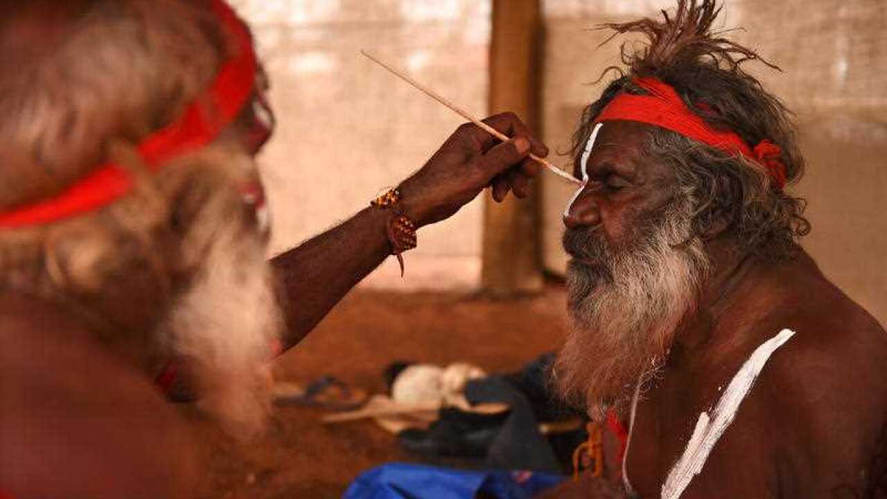 An Aboriginal elder paints a fellow elder before dancing at a cultural event near Uluru, 