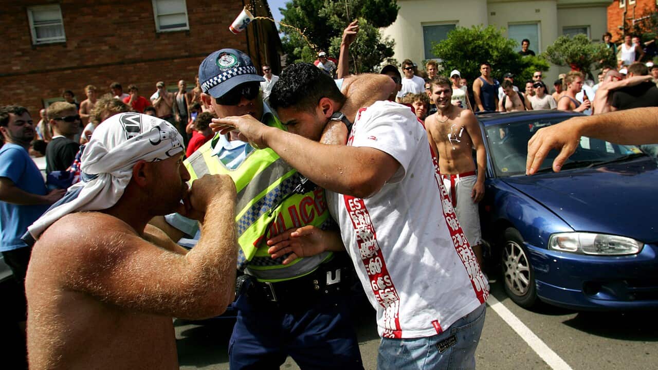 A Dec. 11, 2005 file photo showing a man in a white T-shirt being protected by a police officer while another man (left) tries to punch him after the man in the white T-shirt had been set upon by a crowd at Cronulla beach in Sydney.AAP Image/Paul Miller
