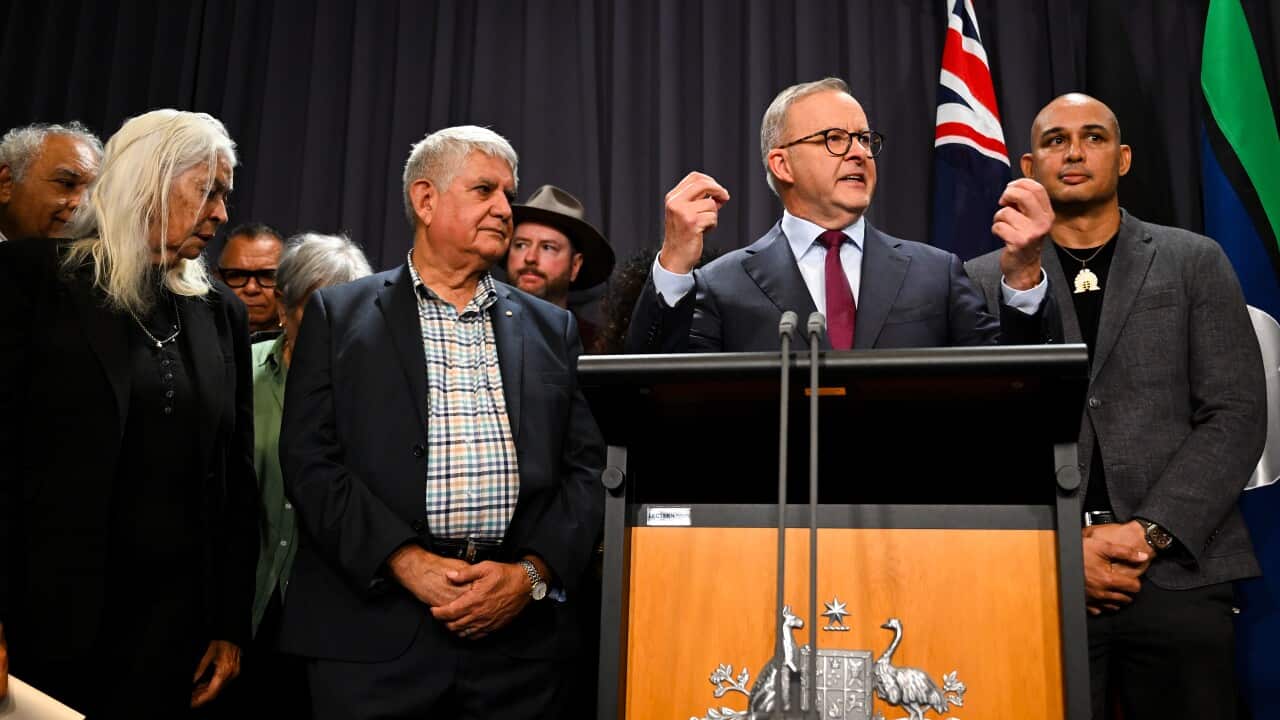 Man speaking at lectern surrounded by supporters.