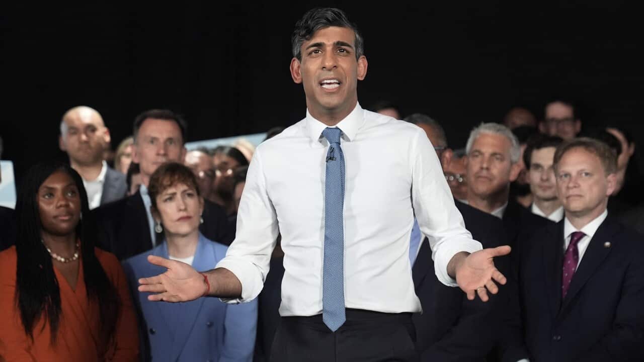 Prime Minister Rishi Sunak stands in front of a crowd, gesturing with his arms to his sides.