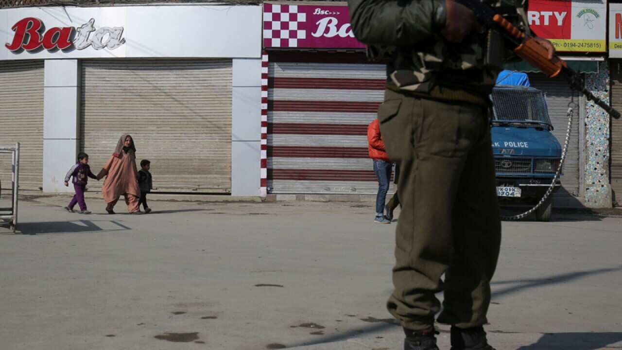 Kashmiri Muslims walk past as an Indian paramilitary soldier