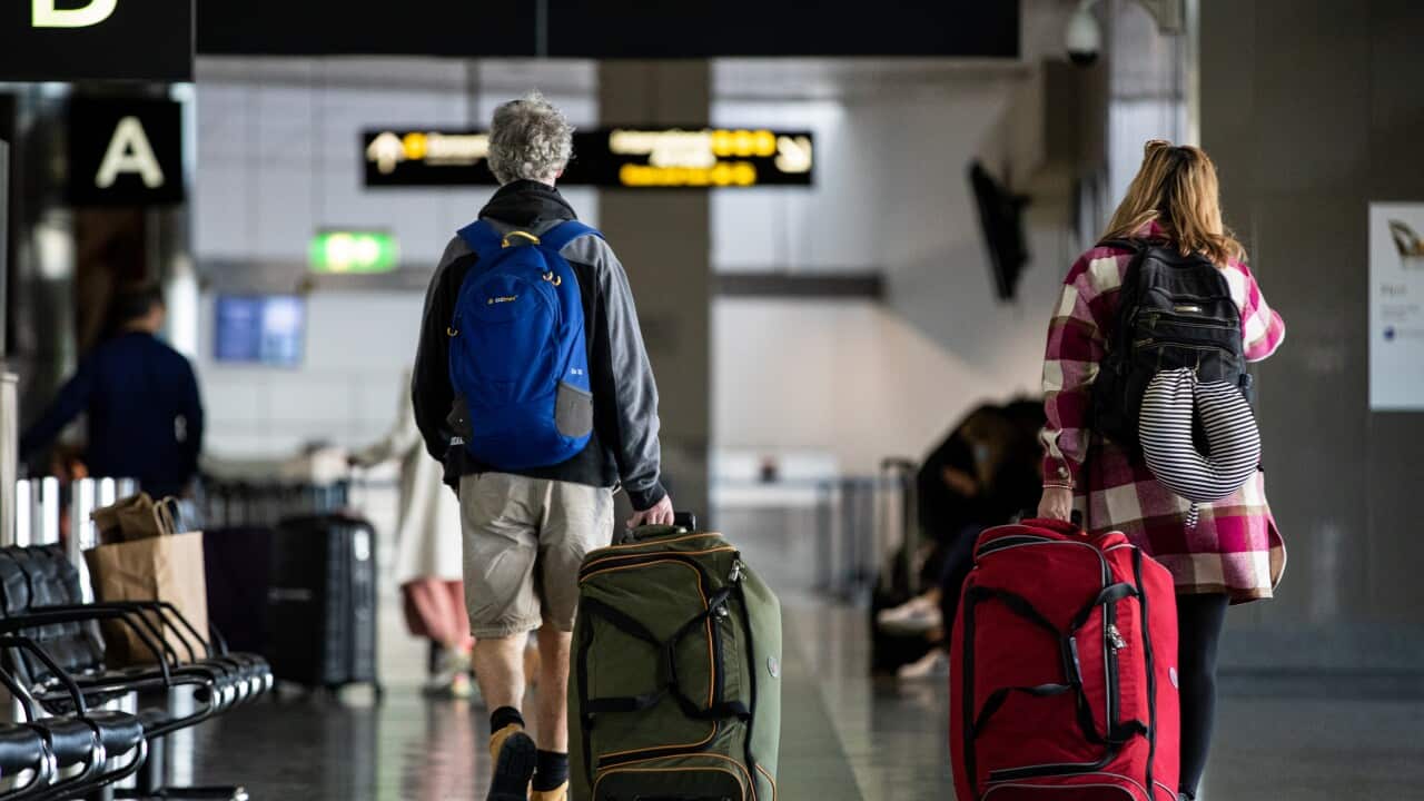 Two people with their backs to the camera, dragging their luggage behind them at the airport.