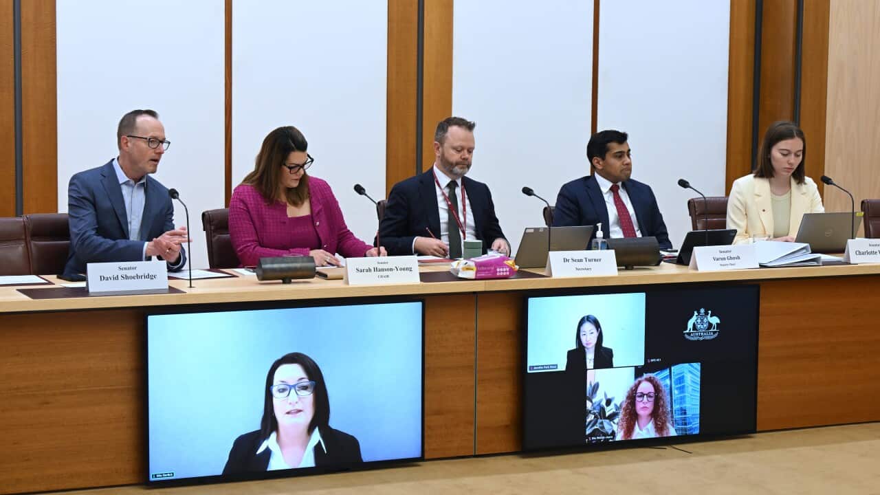 People in suits sitting at a table together. There are television screens on their tables with people on a Zoom call.