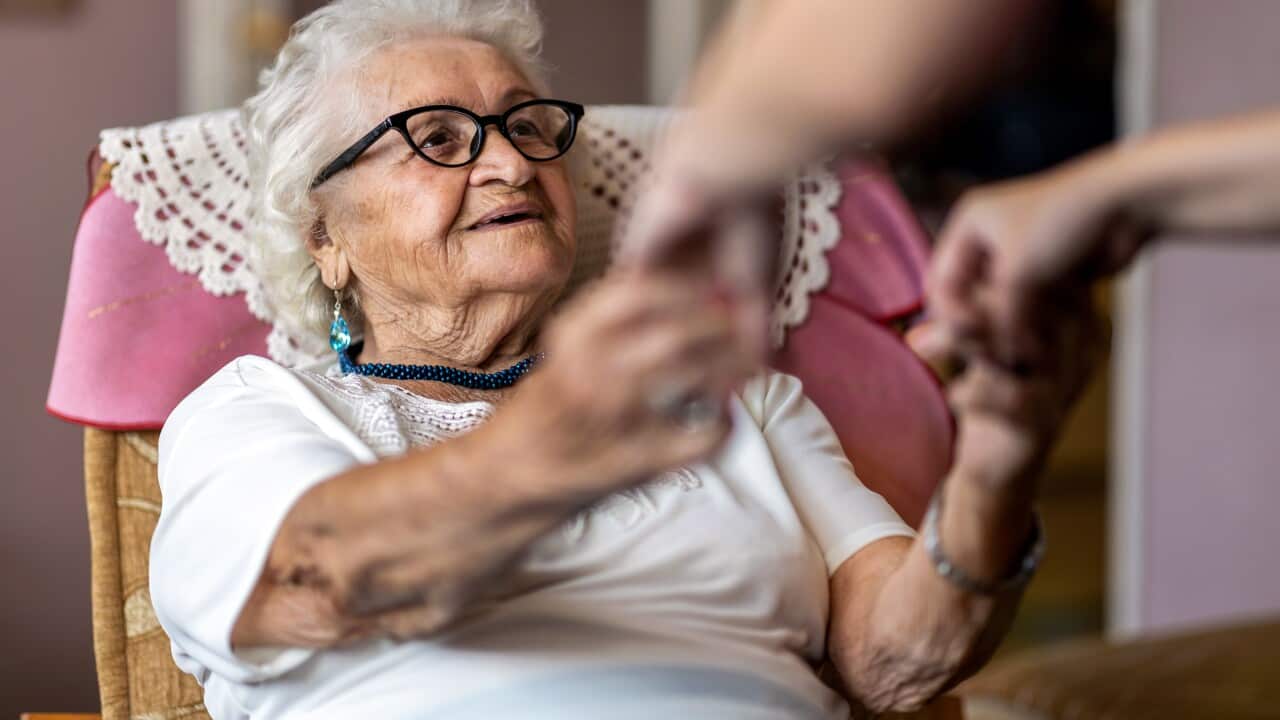 An older woman receives support to stand from a chair