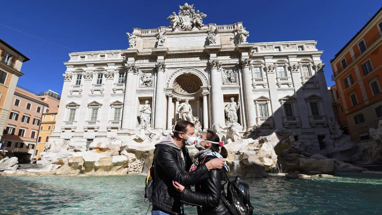 A couple of tourists wearing protective face masks kiss in front of the iconic (and virtually deserted) Fontana di Trevi in Rome, Italy, 12 March 2020.