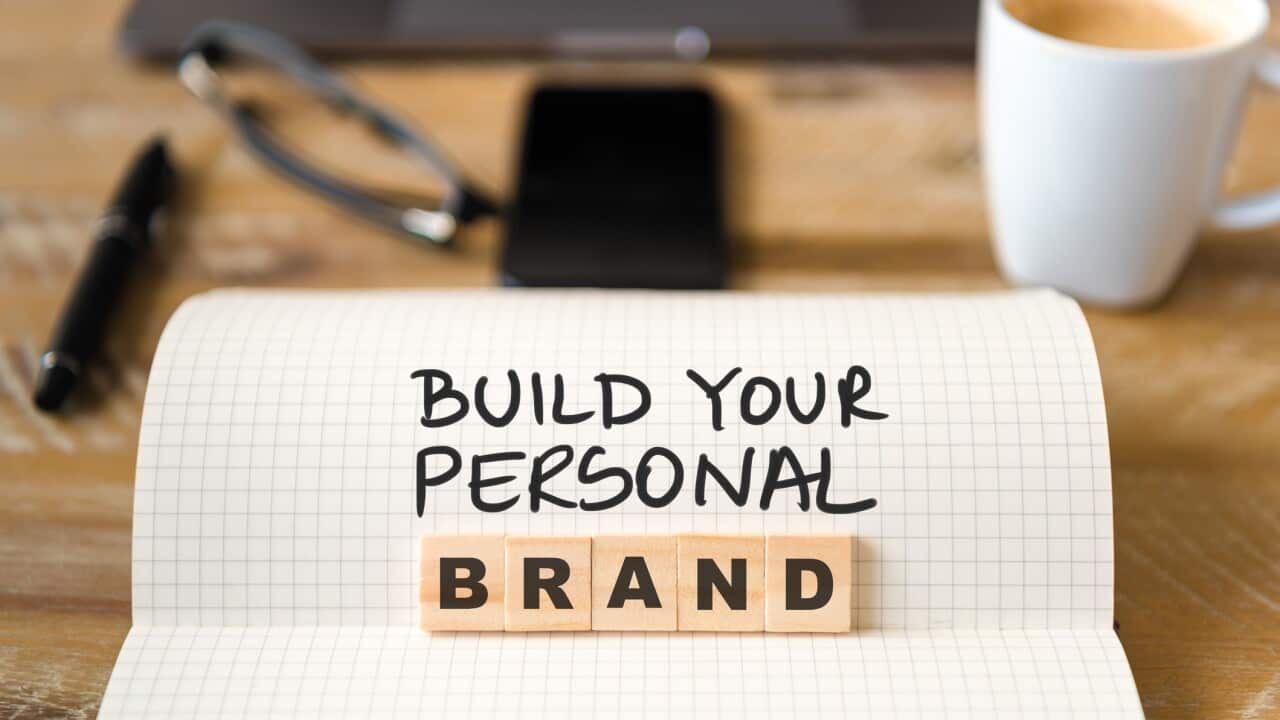Closeup on notebook over vintage desk background, front focus on wooden blocks with letters making Build Your Personal Brand text
