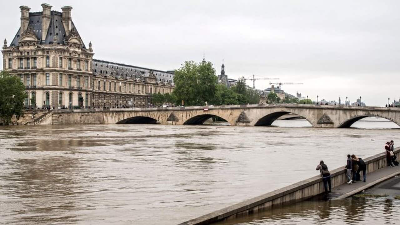 People watch the Louvre museum from a submerged dock